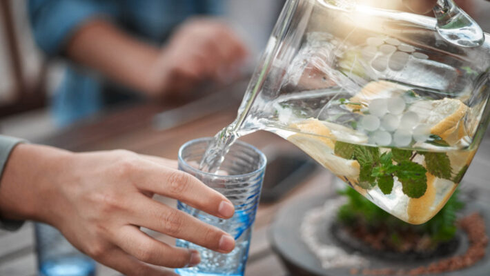Aufnahme einer nicht erkennbaren Person, die um einen Tisch herum Wasser von Sodastream in ein Glas gießt Kalk im Wasser