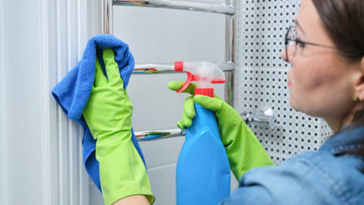 Badezimmer von Kalk befreien - Frau poliert beheizten Handtuchhalter von Kalk befallen und benutzt Säure