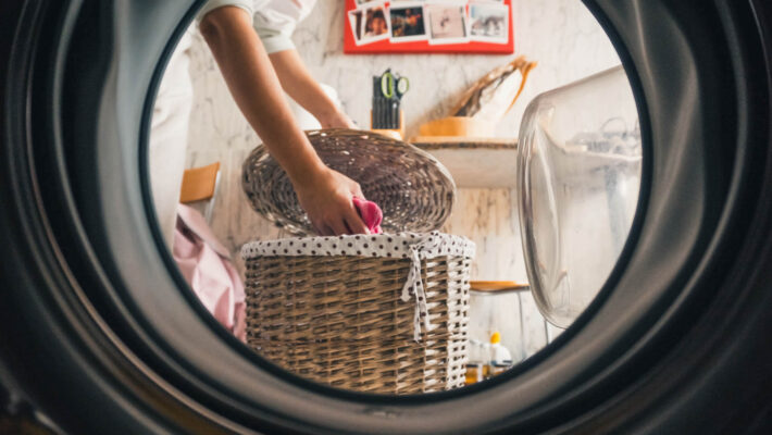 Ein Mädchen nimmt Kleidung aus dem Wäschekorb, um sie in die Waschmaschine zu legen welche mit einem elektronischem Kalkschutz versehen ist