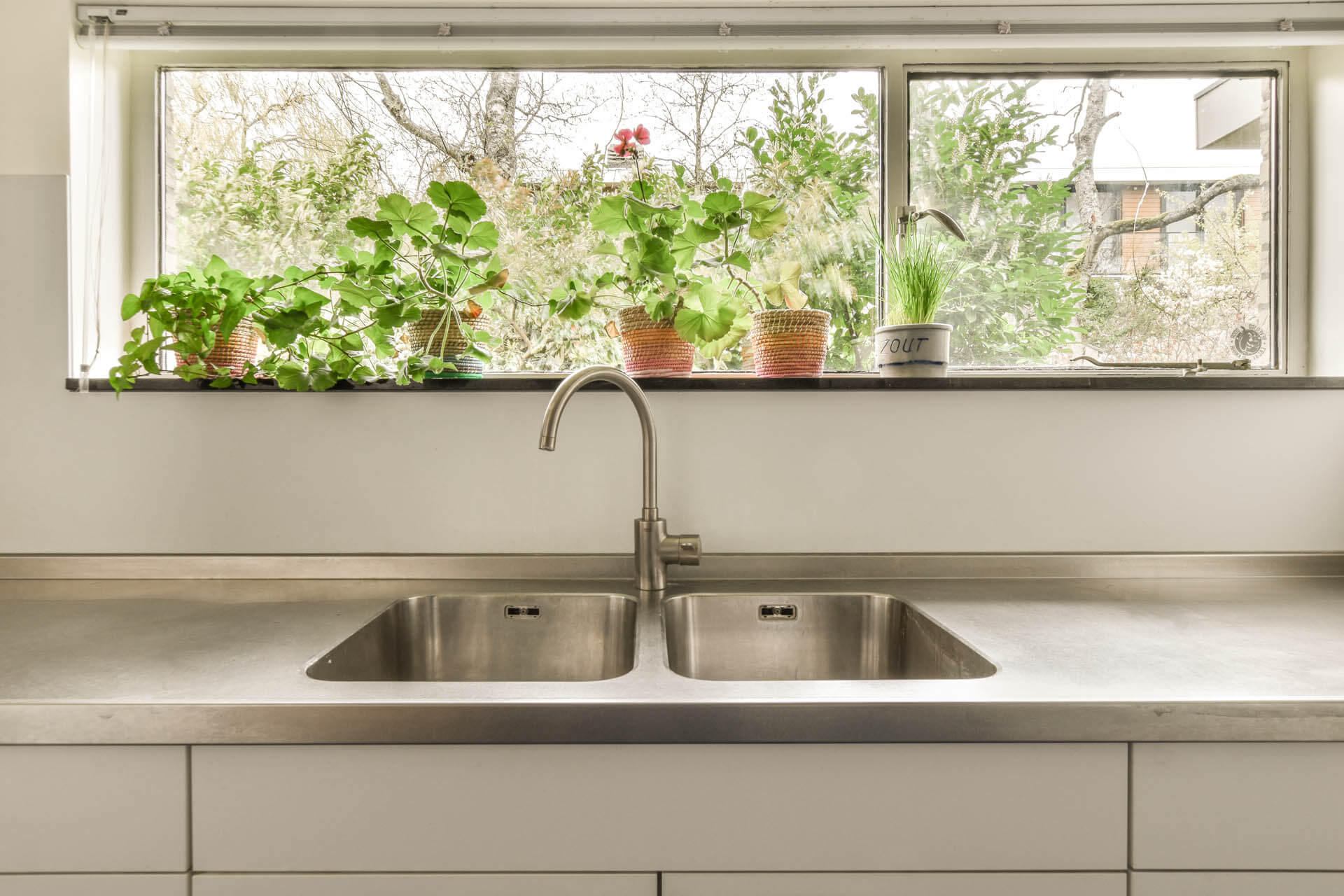 Eine kalkhaltige Küchenspüle vor einem kalkhaltigem Glas mit Pflanzen