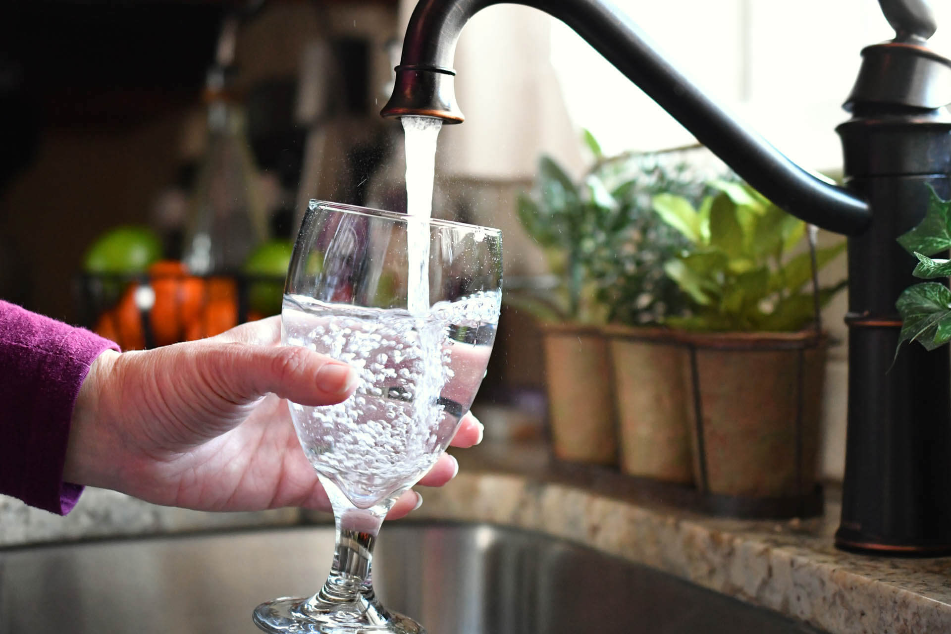 Frau füllt einen Glasbecher mit Kalk im Wasser aus dem Wasserhahn der Küchenspüle da sie den richtigen Salzverbrauch bei ihrer Enthärtungsanlage eingestellt hat