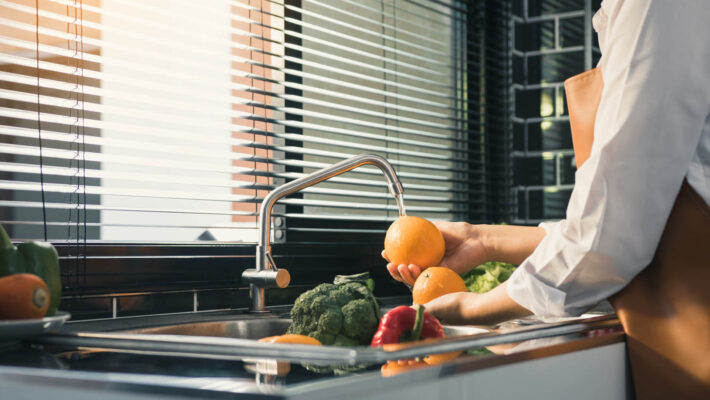 Frau wäscht Obst Orange - Vorbereitung für gesundes Essen in der Küche ohne kalkhaltiges Wasser wegen einem Durchlauferhitzer Kalkschutz