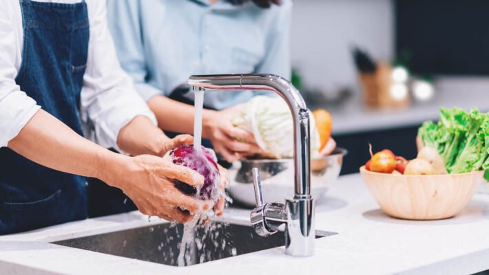 Glückliches Paar, das gemeinsam kocht und Gemüse in der Küche zu Hause mit kalkfreiem Wasser in einem Mineralguss Waschbecken wäscht