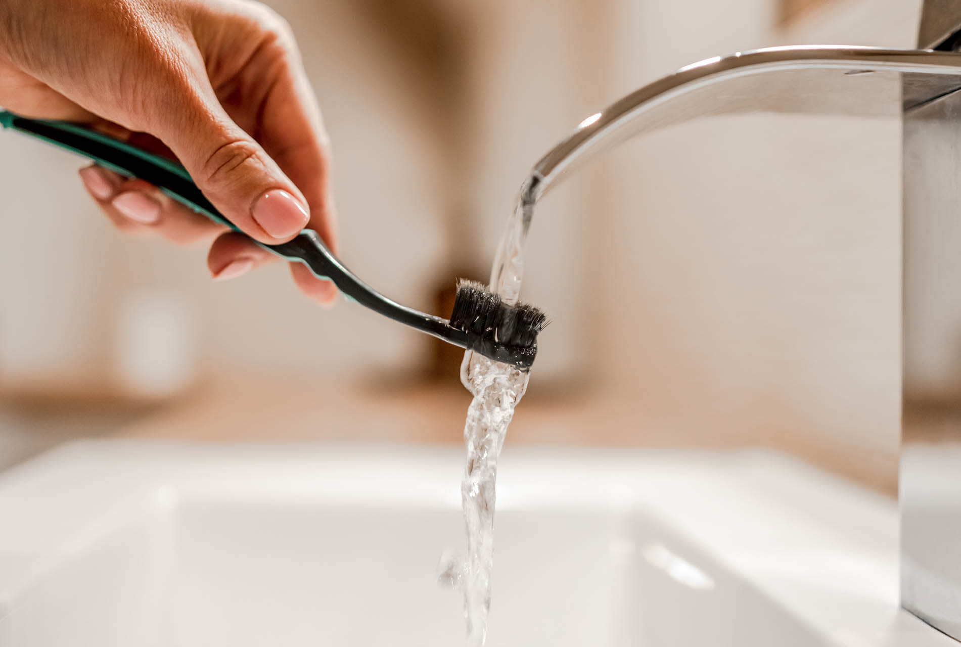 Mädchenhand hält Zahnbürste unter fließendem, kalkhaltigem Wasser